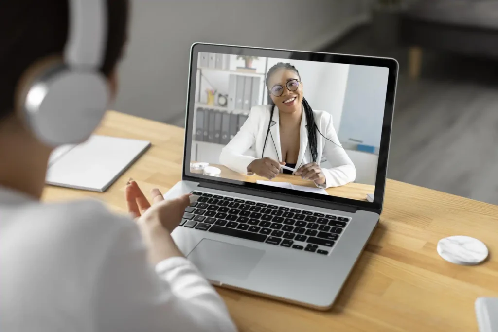 Foto da tela de um notebook de uma pessoa fazendo terapia online com uma psicóloga negra sorrindo.