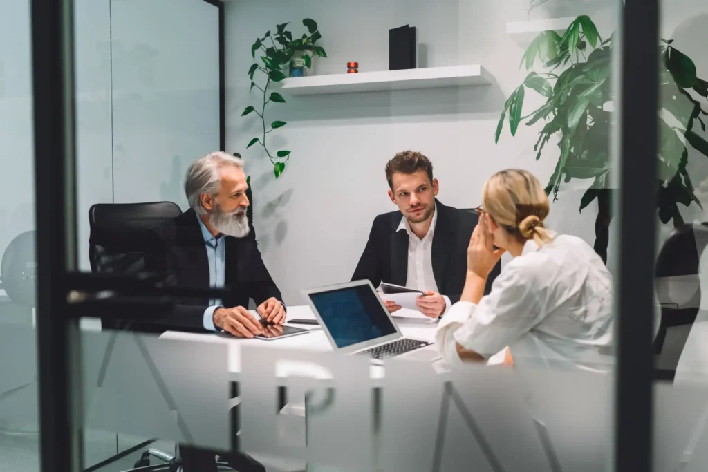 Foto de uma reunião de profissionais de RH (Recursos Humanos) em sala moderna com plantas decorativas e tecnologia, discutindo medidas para implementar a NR-1 na empresa.
