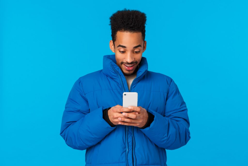 Foto de um homem negro sorridente, usando uma jaqueta azul, com o celular na mão, representando a satisfação dos usuários com um sistema de agendamento de consultas com psicólogos que é fácil de usar.