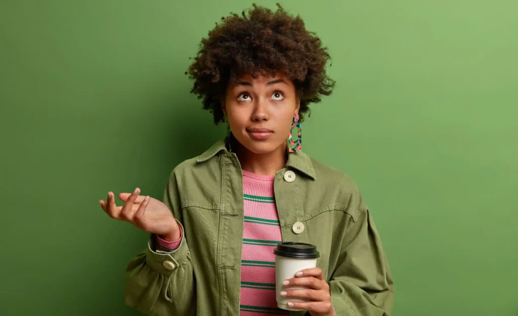 Foto de uma mulher negra, jovem, com cabelo afro, usando jaqueta verde, fazendo gesto de dúvida, ilustrando as incertezas dos pacientes antes de iniciar a terapia.