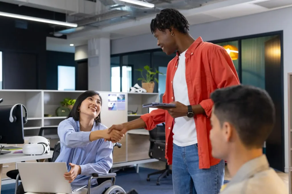 Foto de dois colaboradores, sendo uma mulher asiática com deficiência física e um homem negro, interagindo durante o expediente, demonstrando o respeito às diferenças entre as equipes.