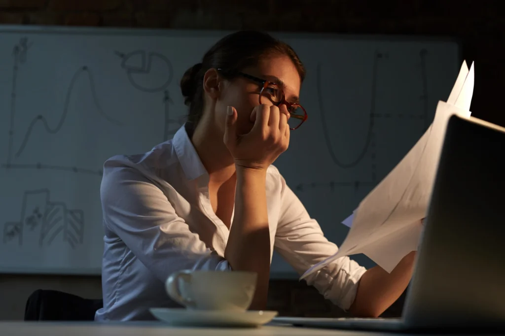 Foto de uma colaboradora olhando para suas tarefas de maneira desmotivada, ilustrando como o presenteísmo pode afetar a rotina de trabalho.