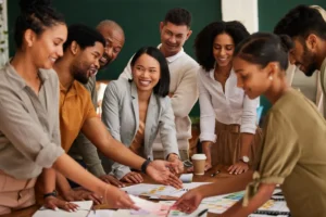 Foto de um grupo de colaboradores diversos reunidos em uma mesa de trabalho, sorrindo e colaborando em um ambiente positivo, representando uma cultura organizacional saudável.