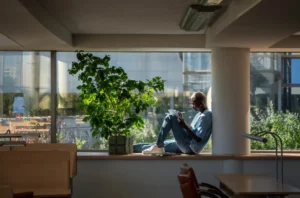 Foto de um colaborador em pausa de leitura em espaço zen corporativo com luz natural e plantas, transmitindo equilíbrio e saúde mental no trabalho.