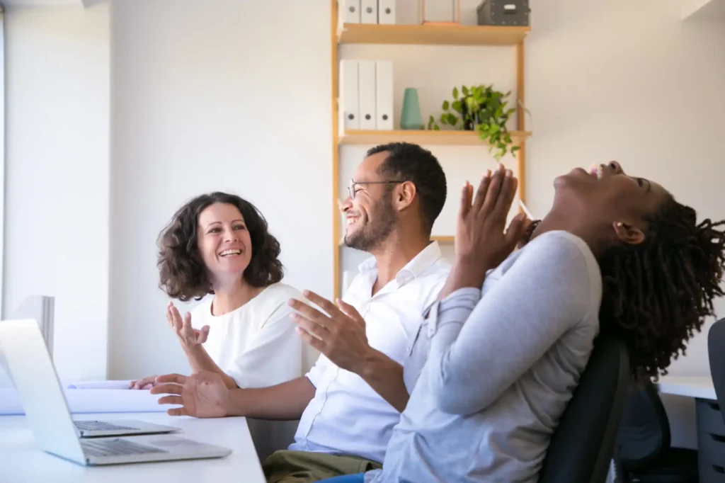 Foto de uma equipe diversa e entrosada, mantendo um relacionamento divertido e respeitoso entre os colaboradores, estimulado pela cultura organizacional da sua empresa, que investiu em espaços zen para a melhora na saúde mental no trabalho.